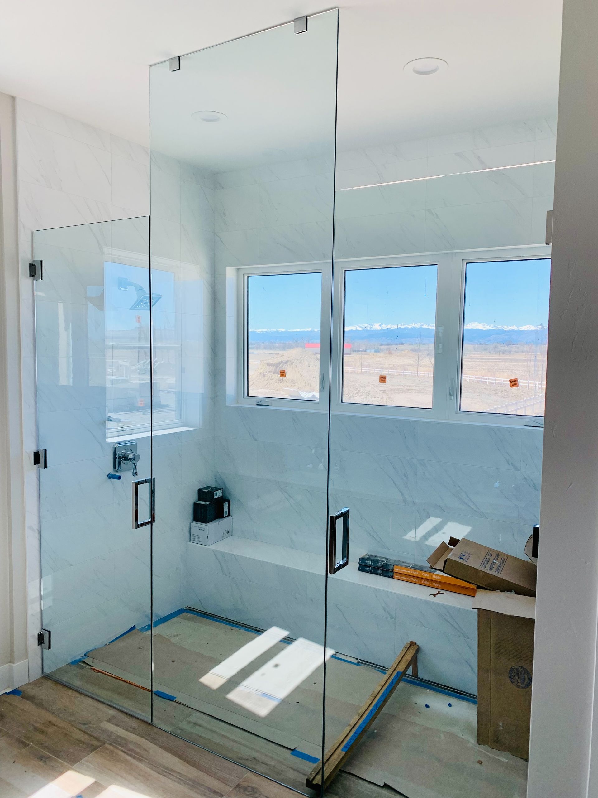 Glass shower enclosure in a bright, modern bathroom with mountain views through large windows.