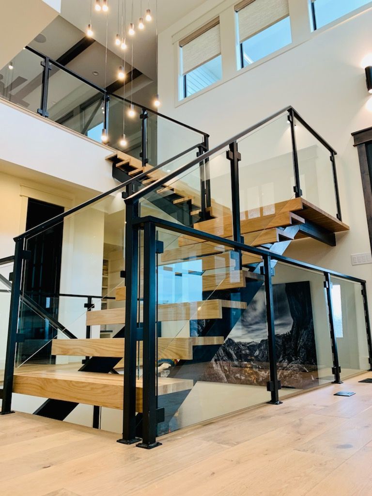 Modern staircase with black metal railing, glass panels, and wooden steps in a bright interior.
