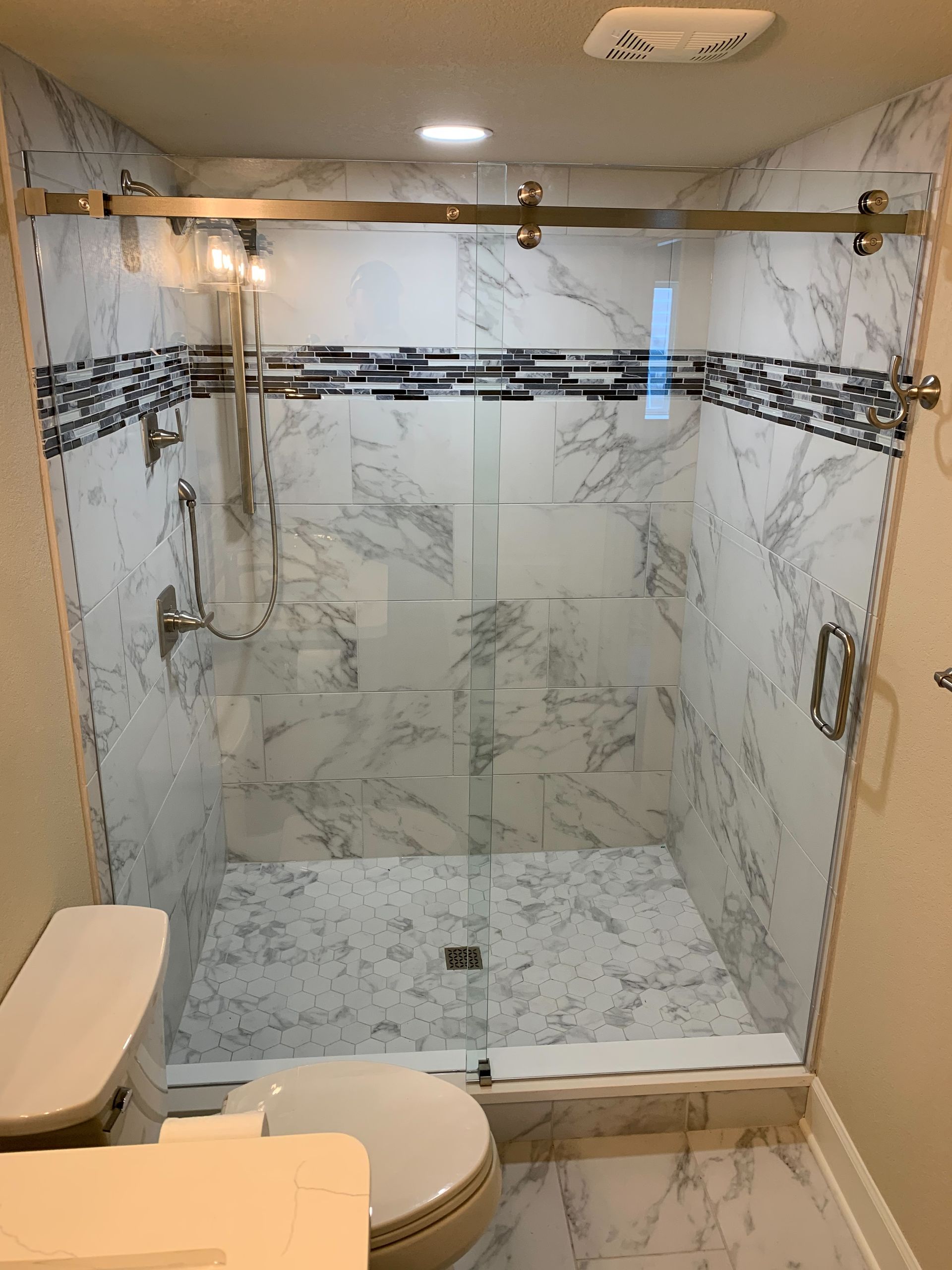 Bathroom with glass-enclosed shower, marble-look tile, and toilet in foreground.