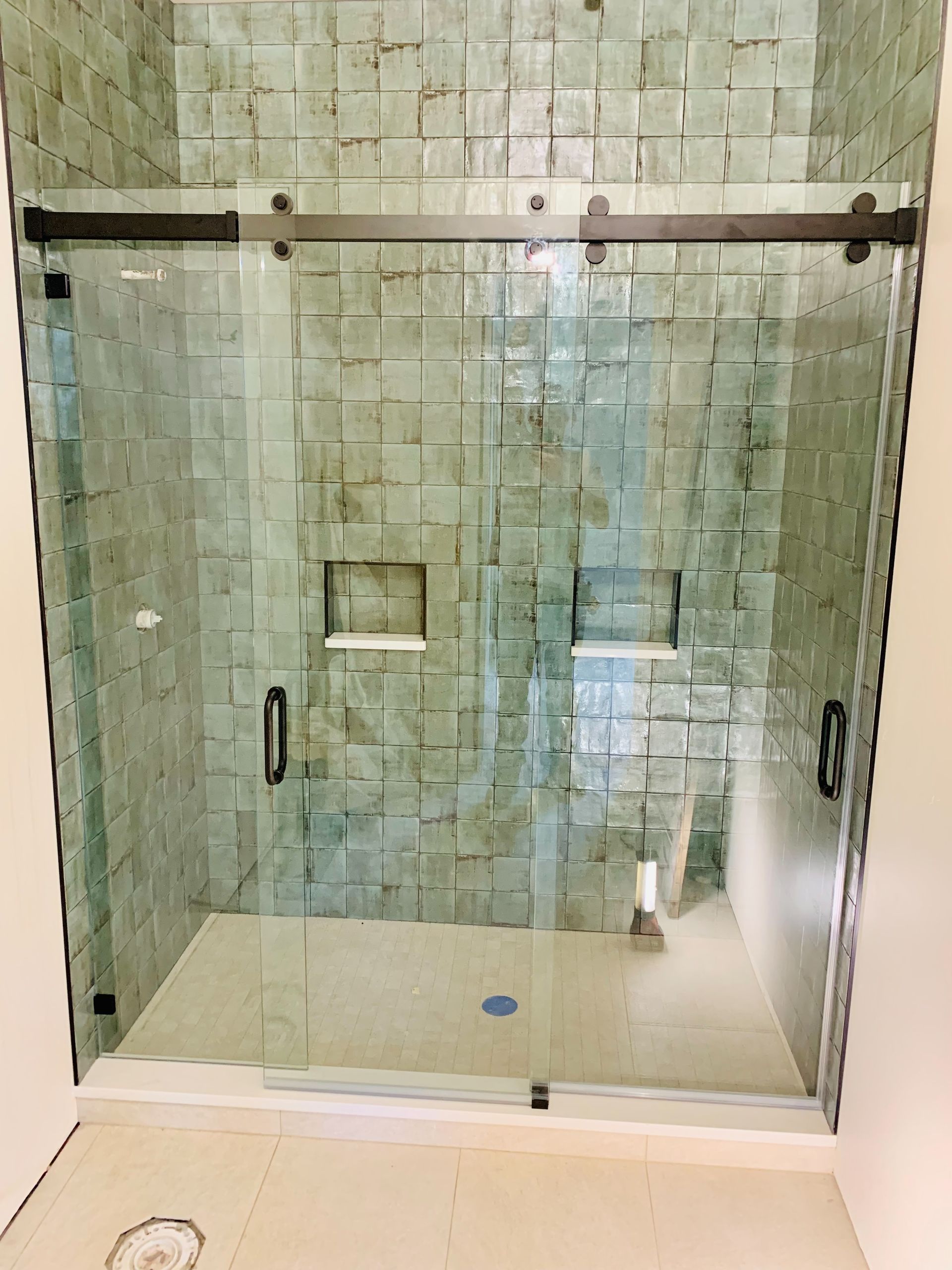 Glass shower enclosure with green tiled walls and clear doors in a bathroom