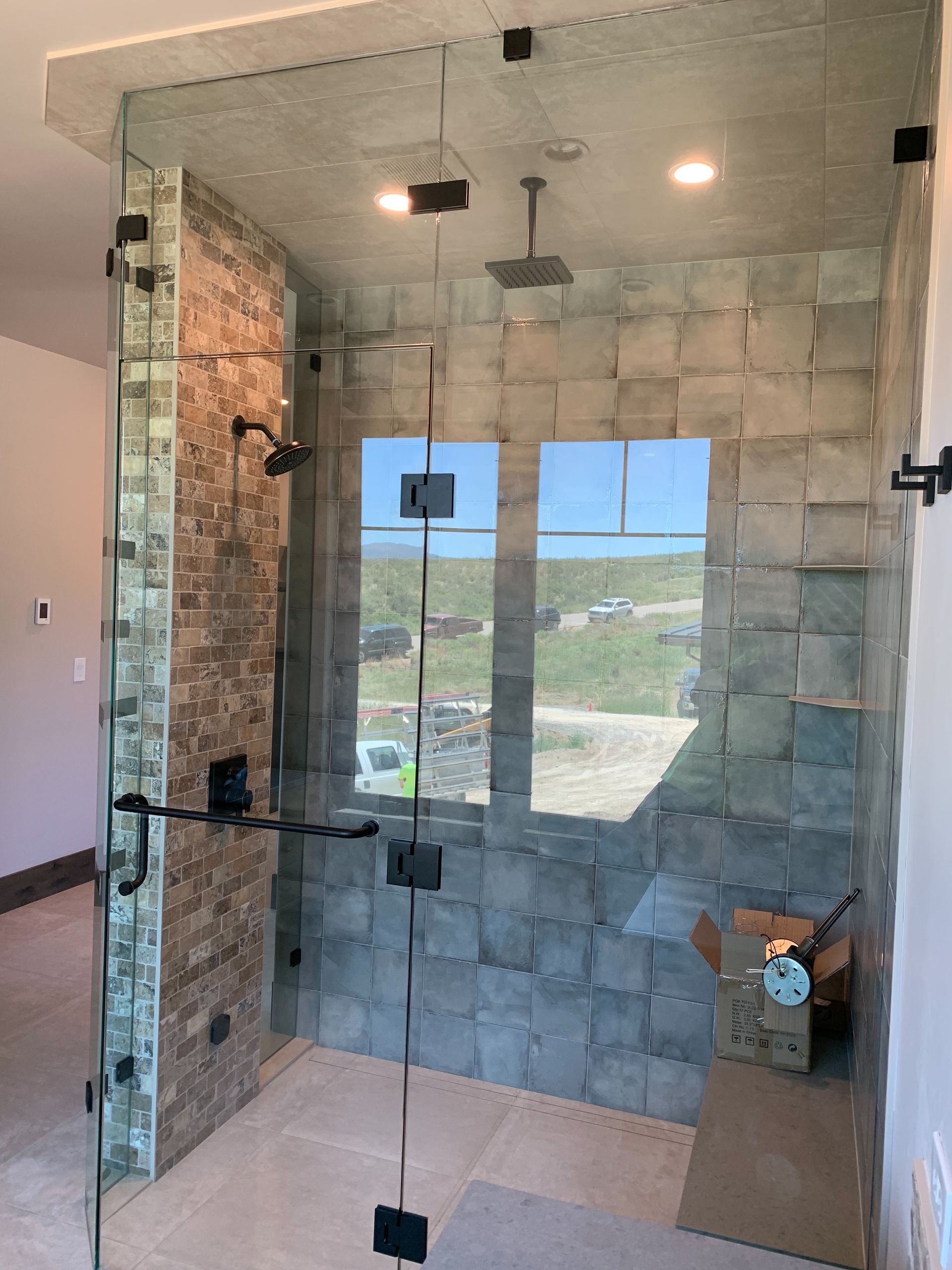 Glass shower enclosure in a tiled bathroom with a view outside through the doors.