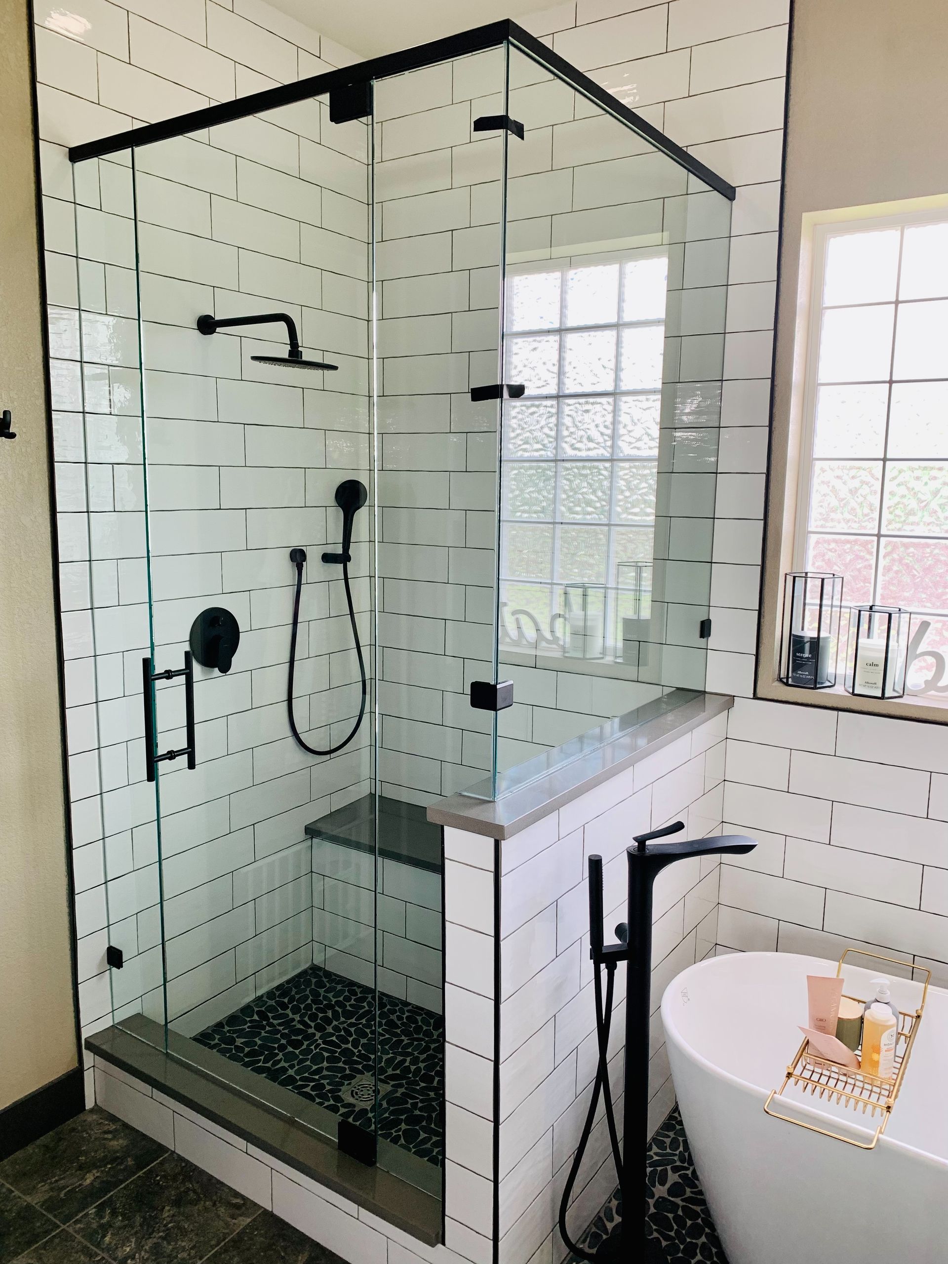 Black-framed glass shower with white subway tiles and rainfall showerhead in a bright bathroom