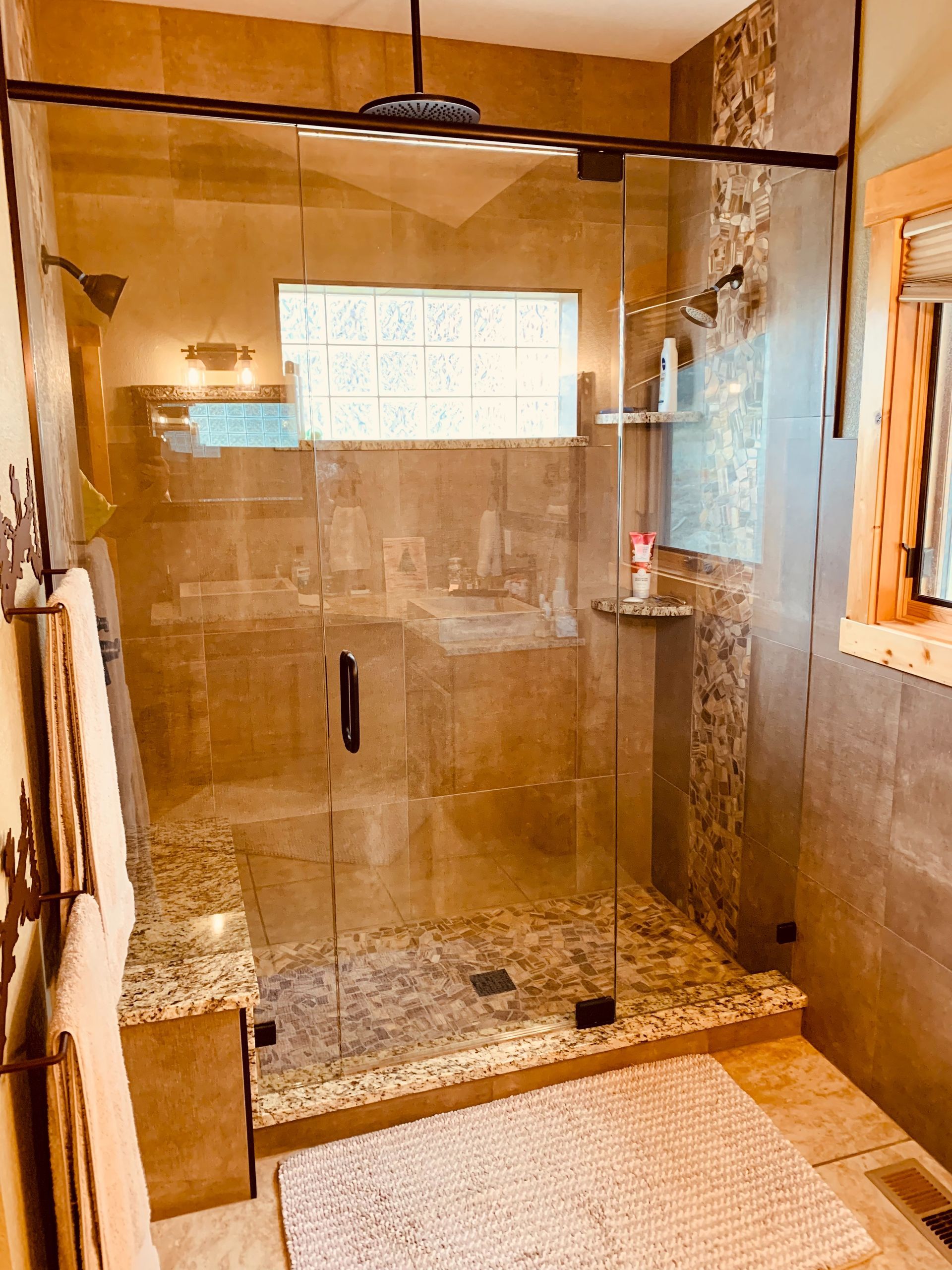 Glass walk-in shower with tan tile, bench, and mosaic pebble floor in a modern bathroom