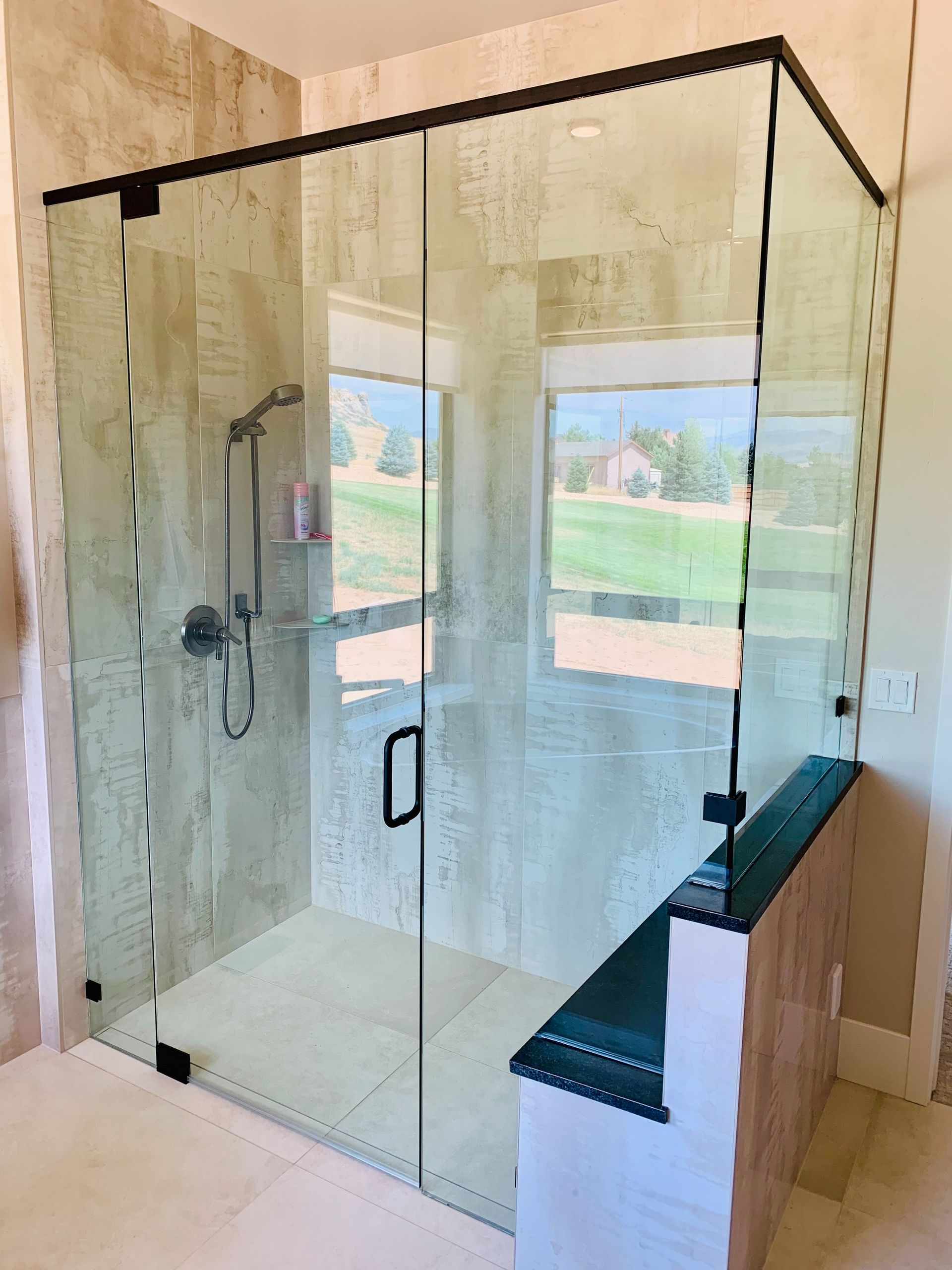 Glass walk-in shower with black trim and built-in bench in a bright bathroom