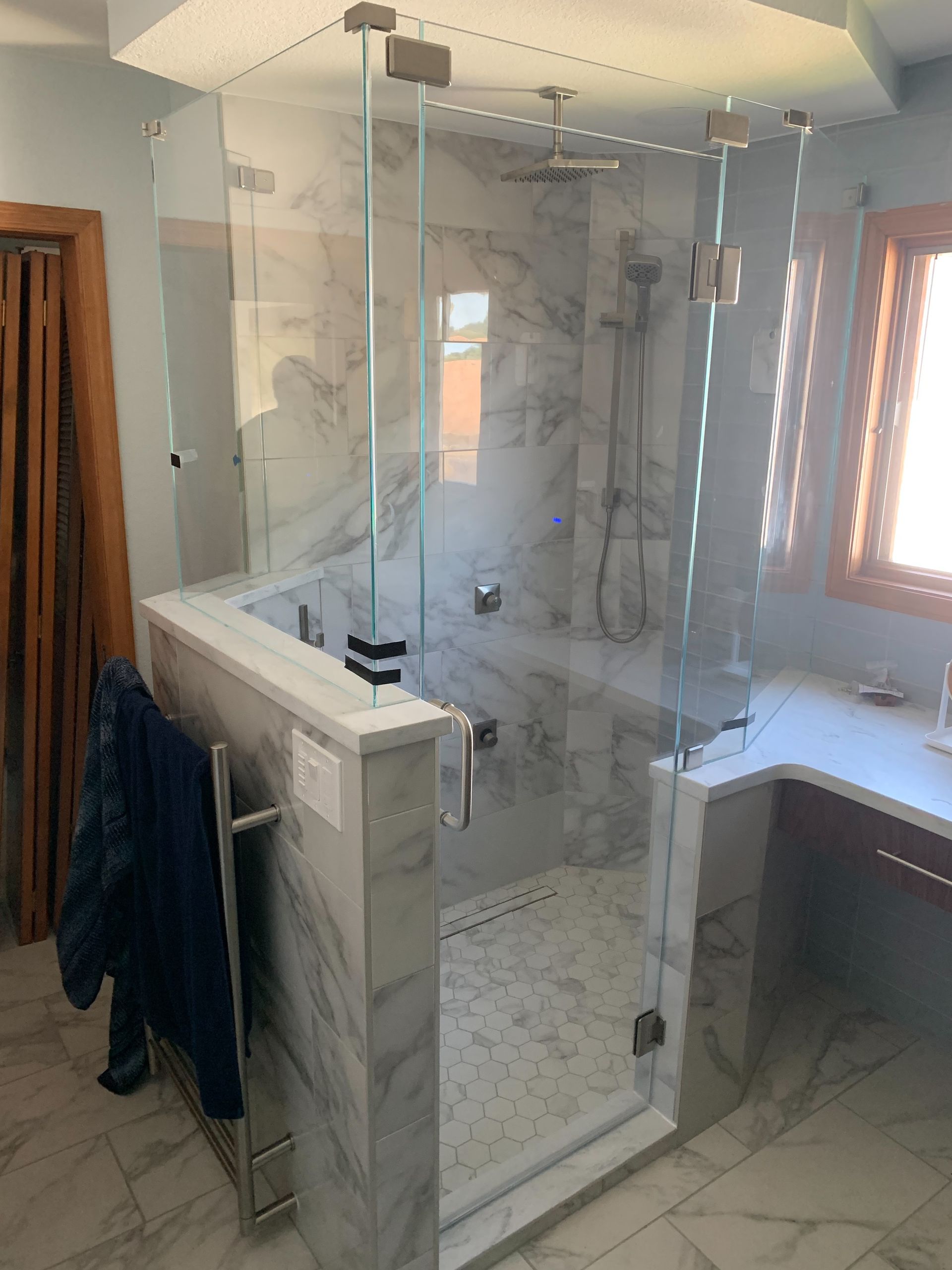 Glass shower enclosure in a tiled bathroom with a marble vanity and window light
