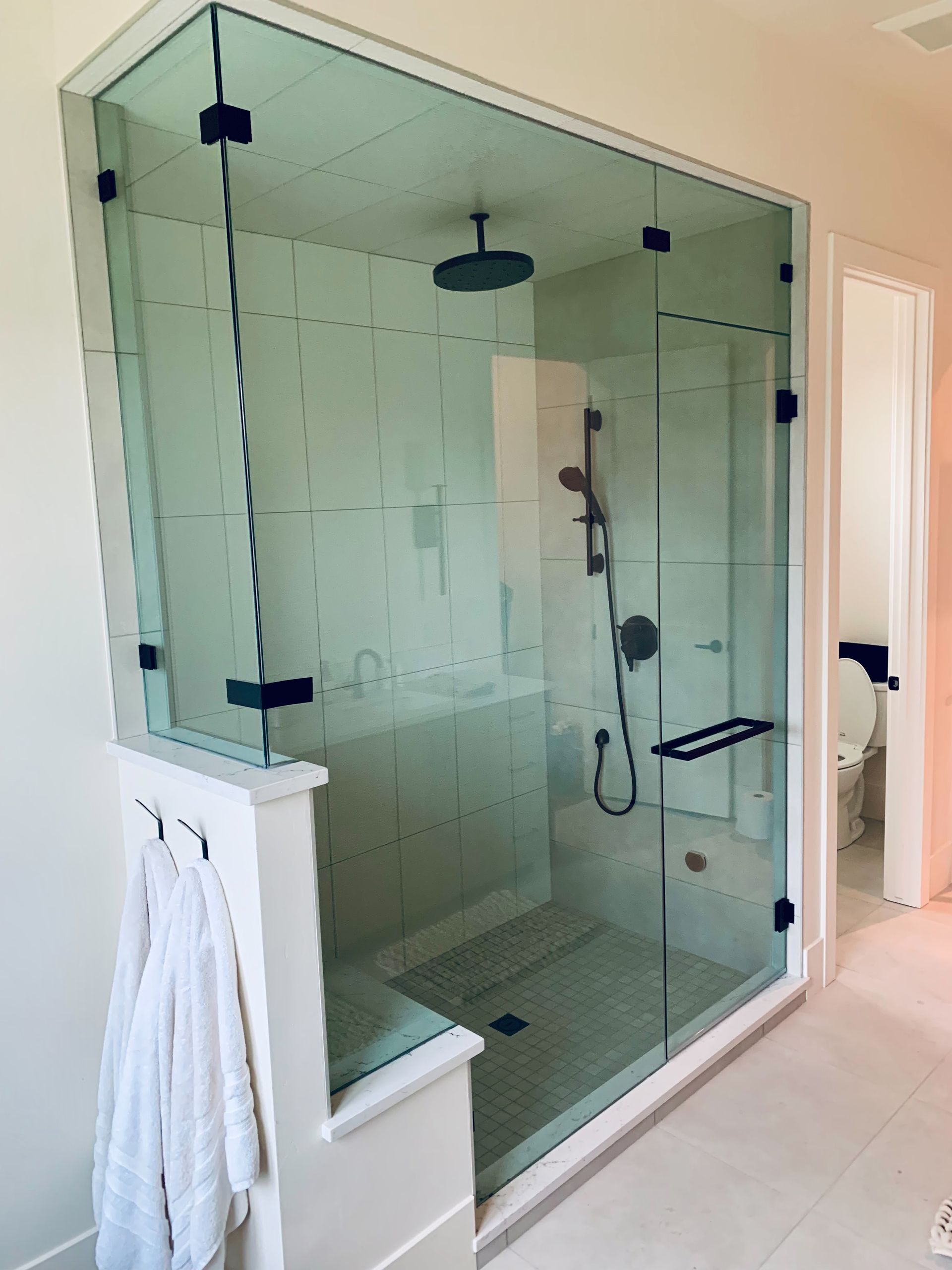 Glass walk-in shower with black fixtures and white tiled bathroom interior