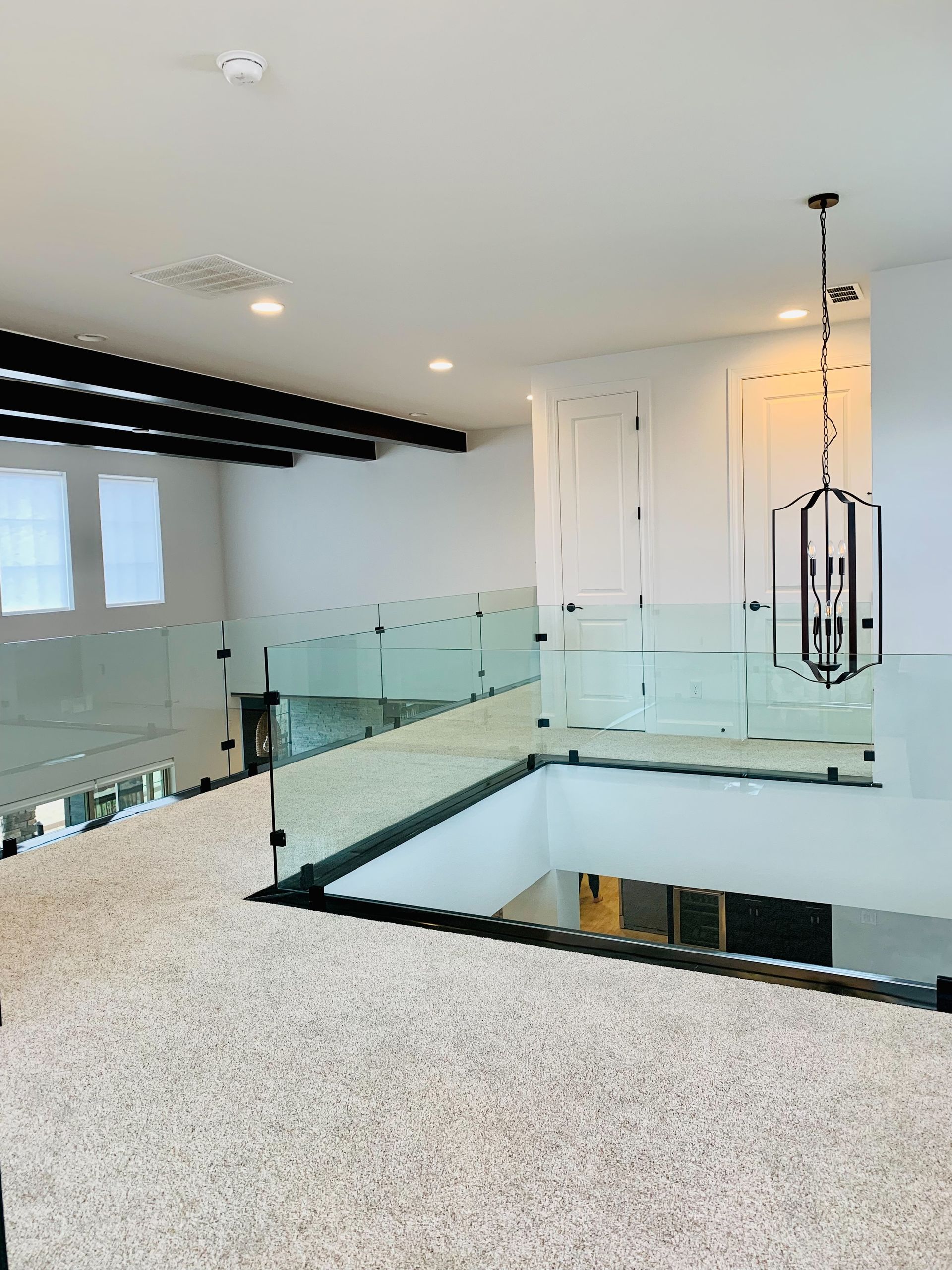 Modern bright interior with glass railings, white walls, and a black-framed stairwell opening