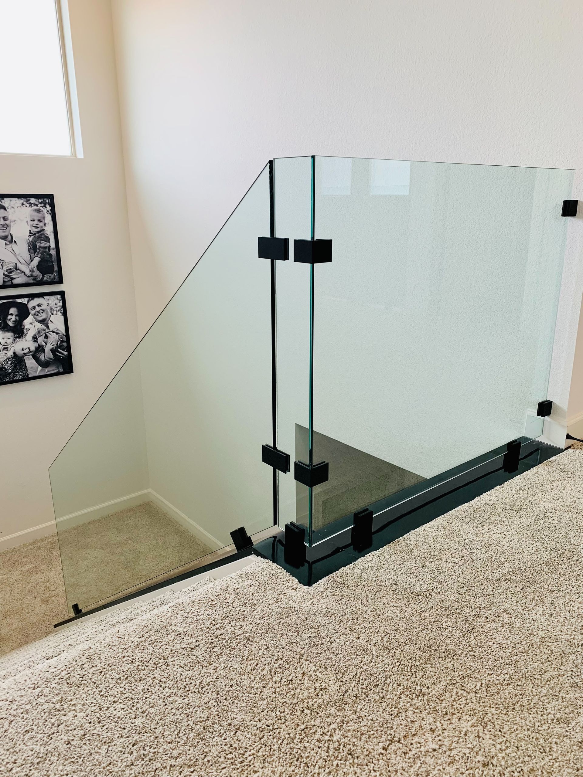 Glass staircase railing with black metal hinges on a carpeted landing
