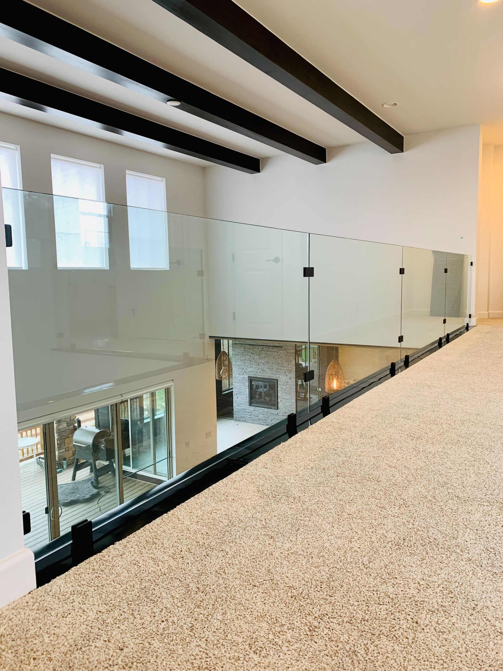Modern indoor balcony with glass railing, white speckled floor, and exposed ceiling beams