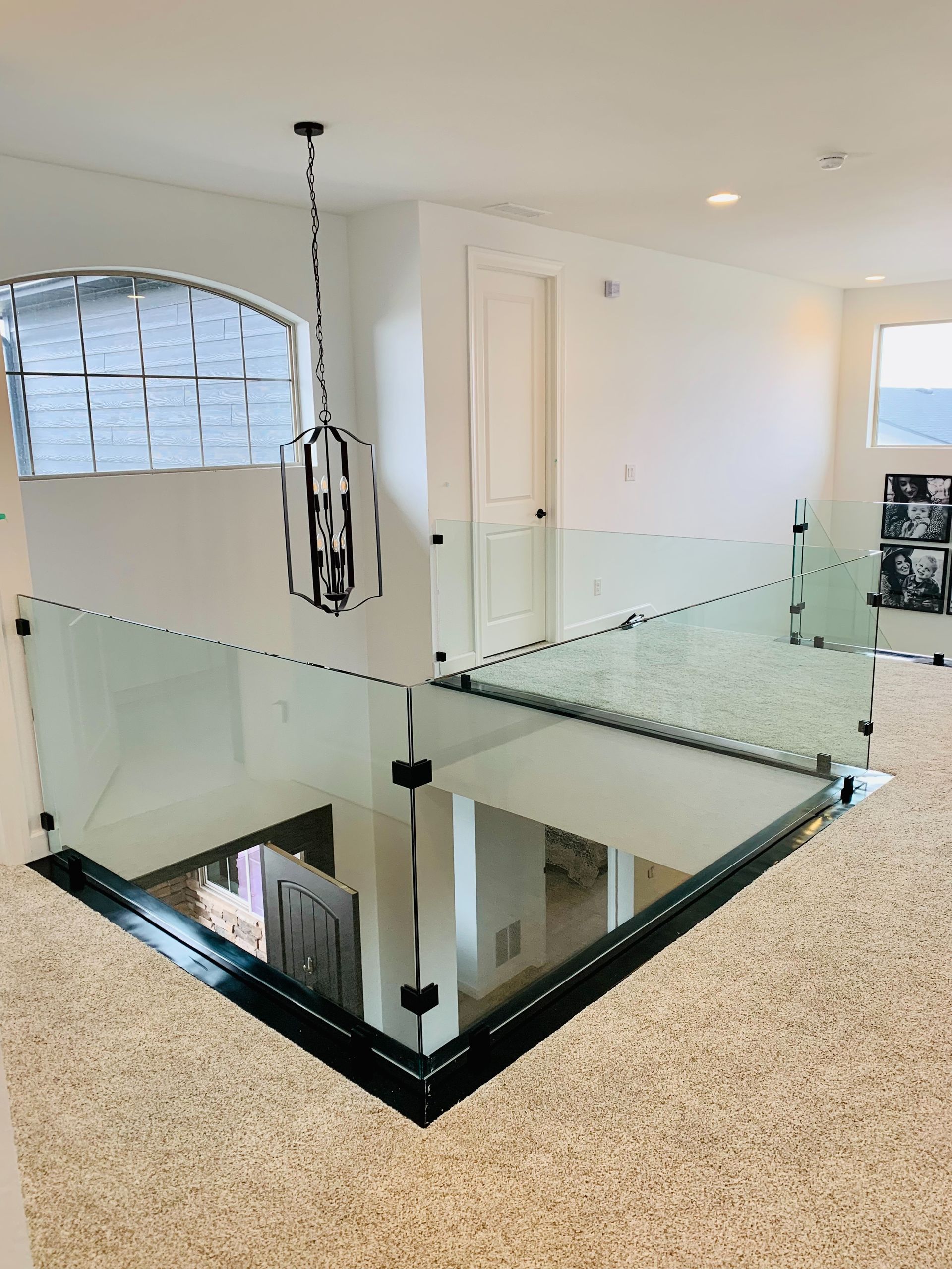 Modern interior landing with glass railing, black-framed opening, and light carpeted floor