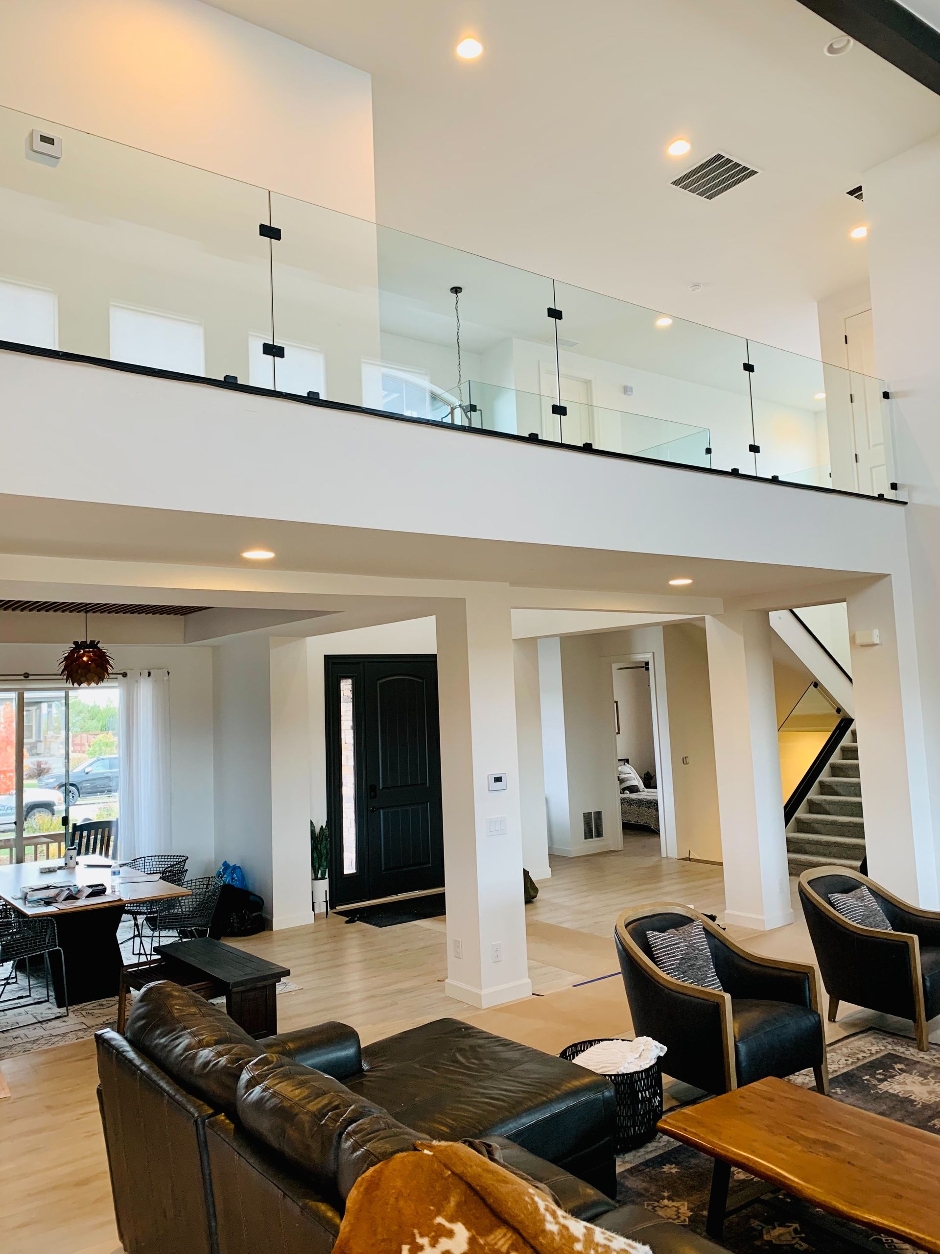 Modern open-plan living room with leather sofas, stairs, and a glass-railed mezzanine in a bright interior