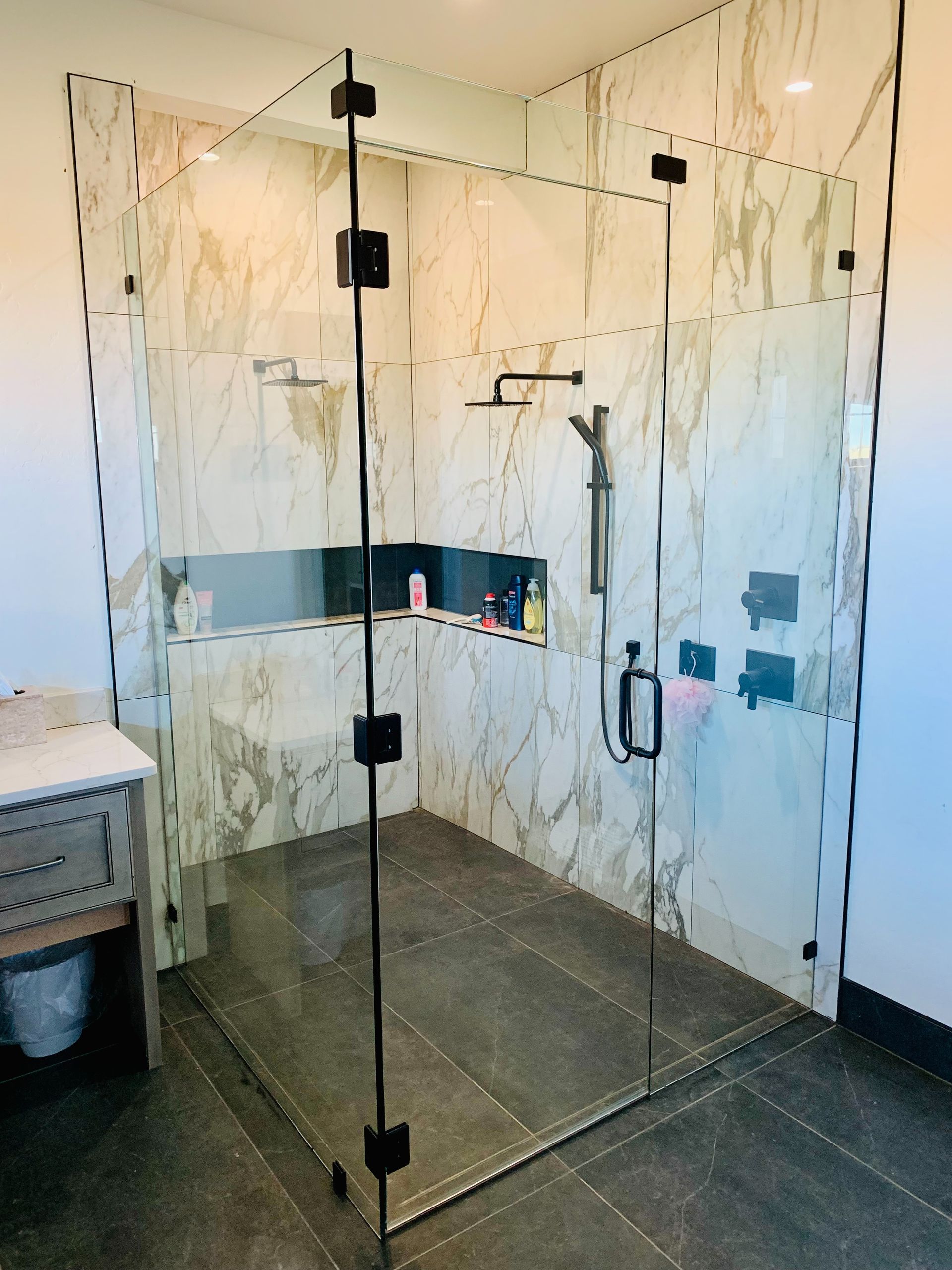 Glass walk-in shower with dark tile floor and marble-look walls