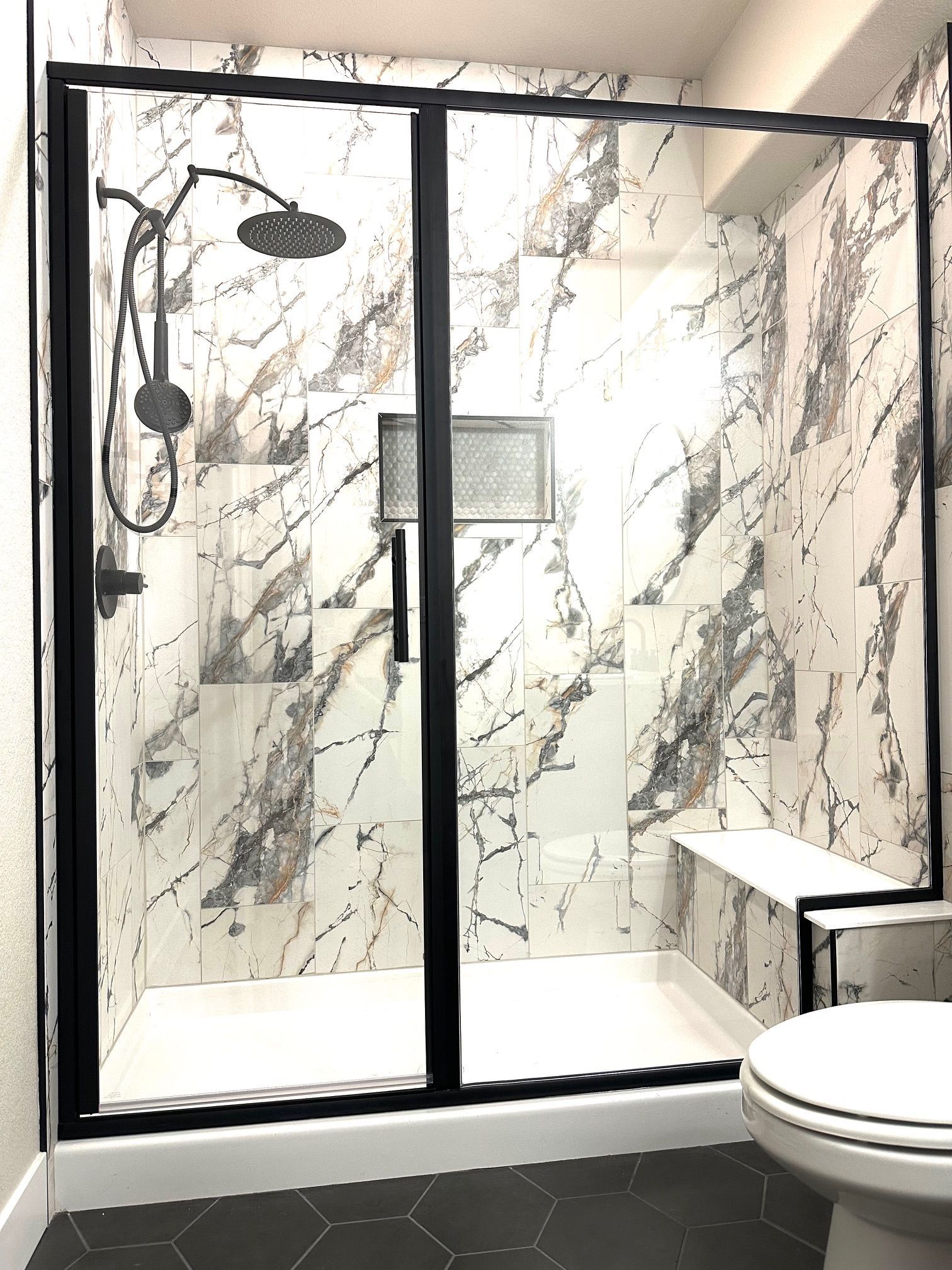 Modern bathroom with a black-framed walk-in shower, marble-look tile, and a toilet in the foreground