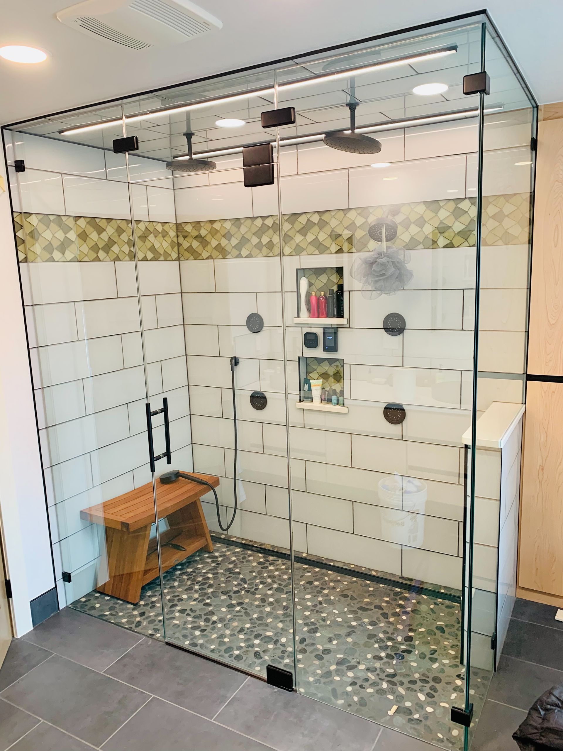 Glass walk-in shower with white tiled walls, pebble floor, and wooden bench.