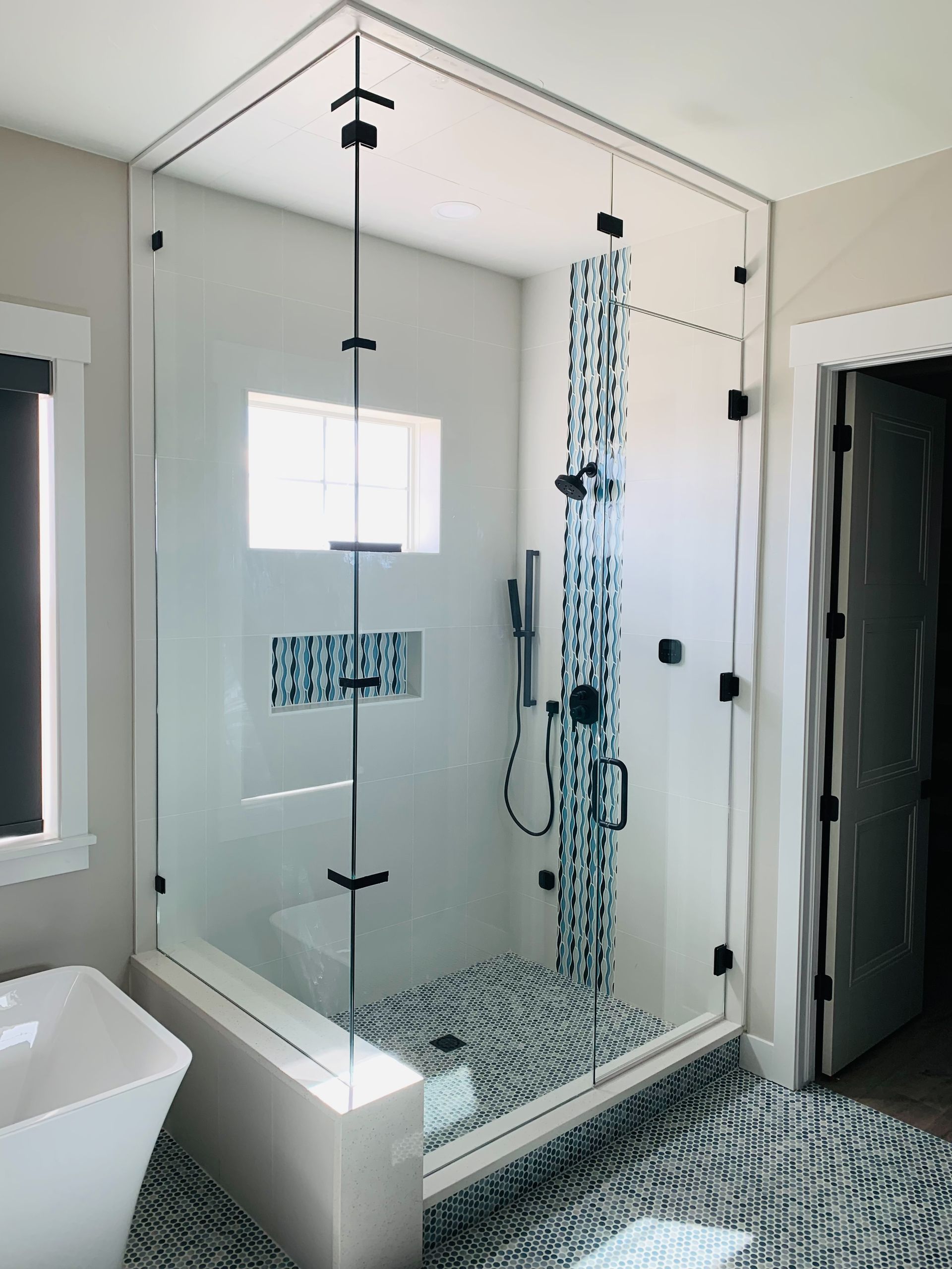 Modern bathroom with glass walk-in shower, mosaic tile floor, and built-in tub beside a window.