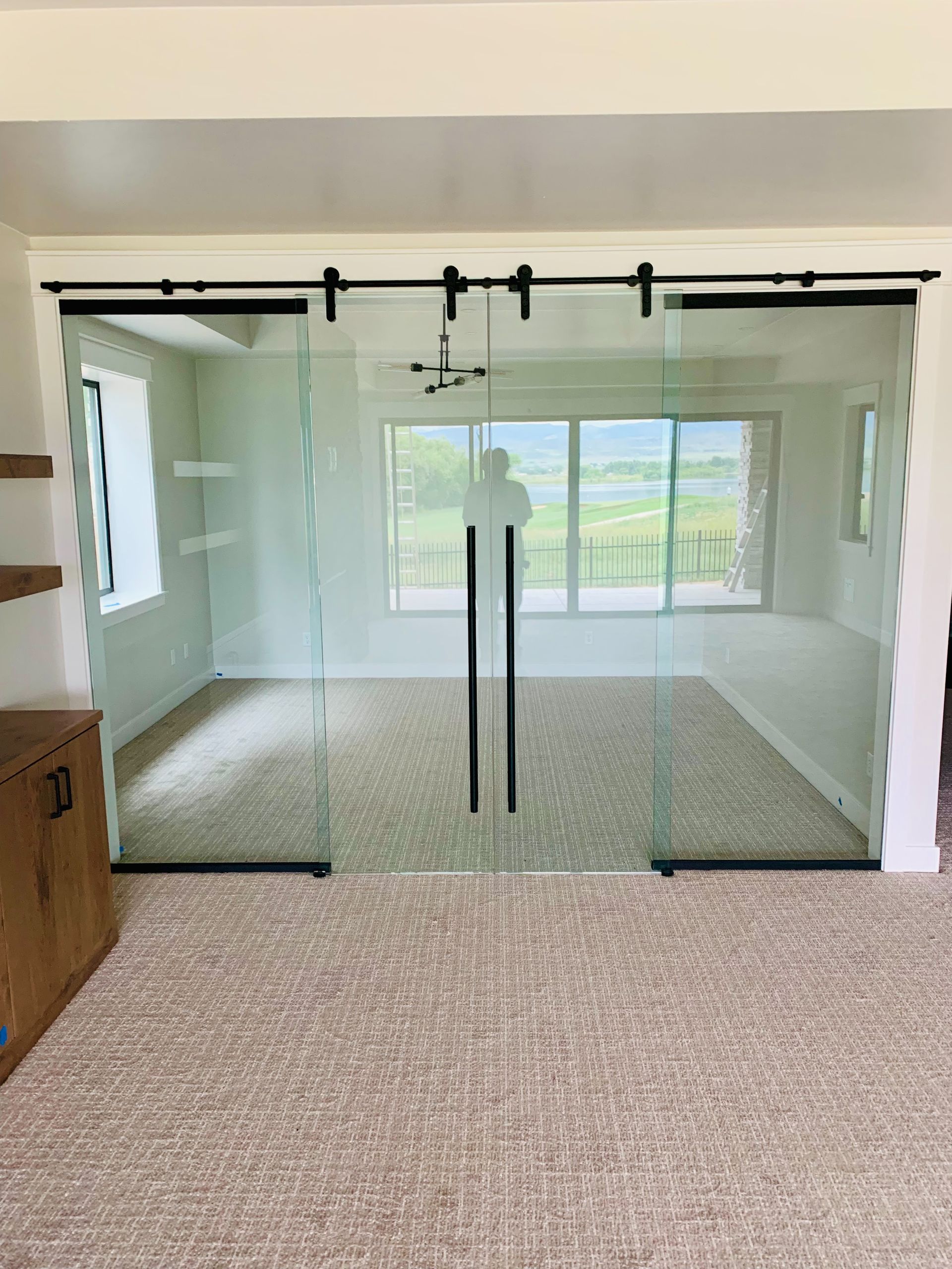 Glass sliding doors with black handles opening to a bright room with carpet and large windows.