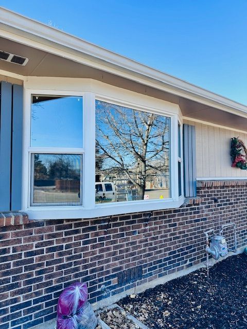 Brick house exterior with a bay window, beige siding, and a wreath on the wall