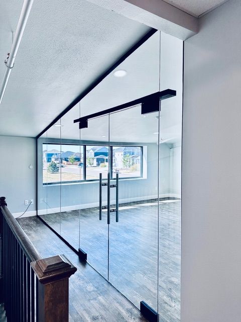 Empty modern room with glass partition doors, gray tile floor, and large windows letting in daylight
