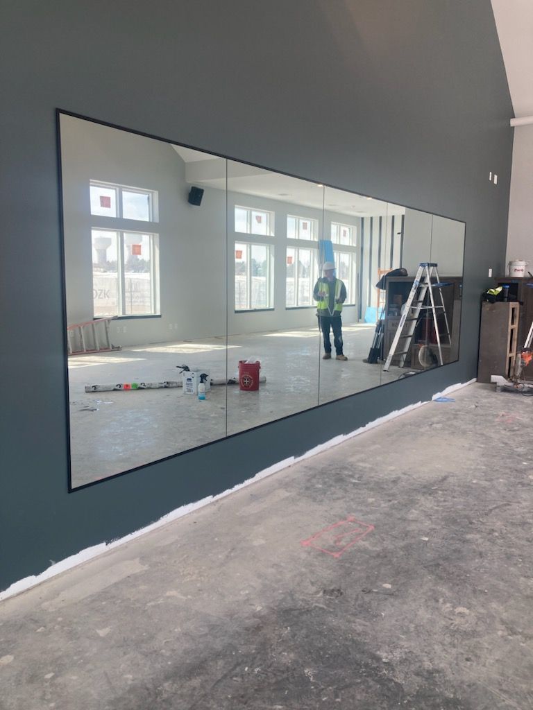 Large wall mirror in an unfinished room, reflecting windows and a worker in a neon vest.