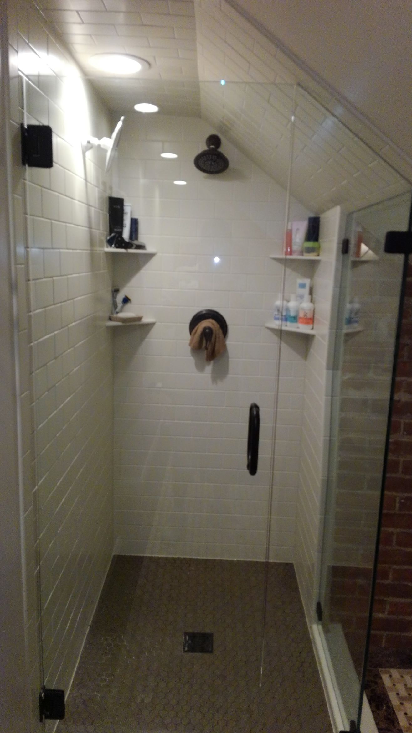 Small tiled shower stall with white walls, a black showerhead, shelves, and a drain in the floor.