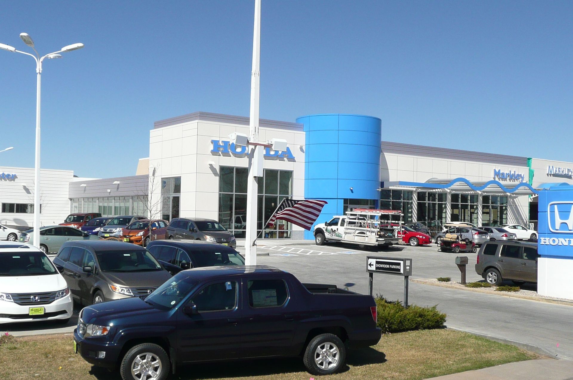 Car dealership lot with parked cars, a blue building, and a Honda sign under a clear sky