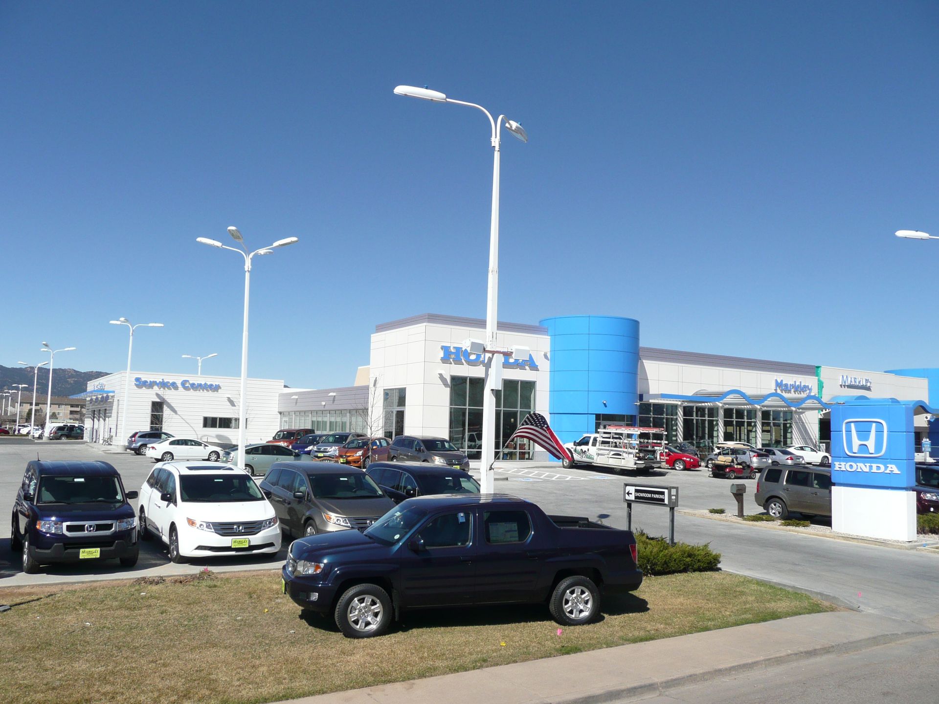 Car dealership lot with parked cars, a white building, and a blue sign under a clear sky