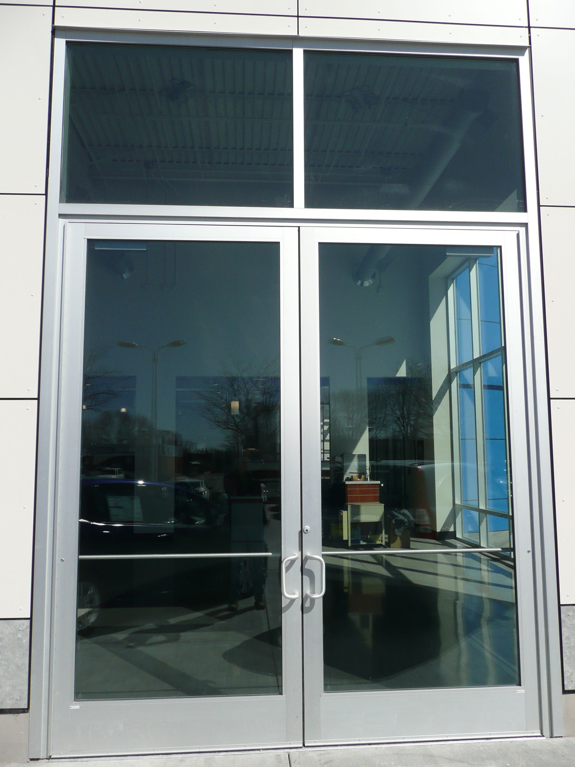 Glass double doors with metal handles at a building entrance, reflecting the outdoors