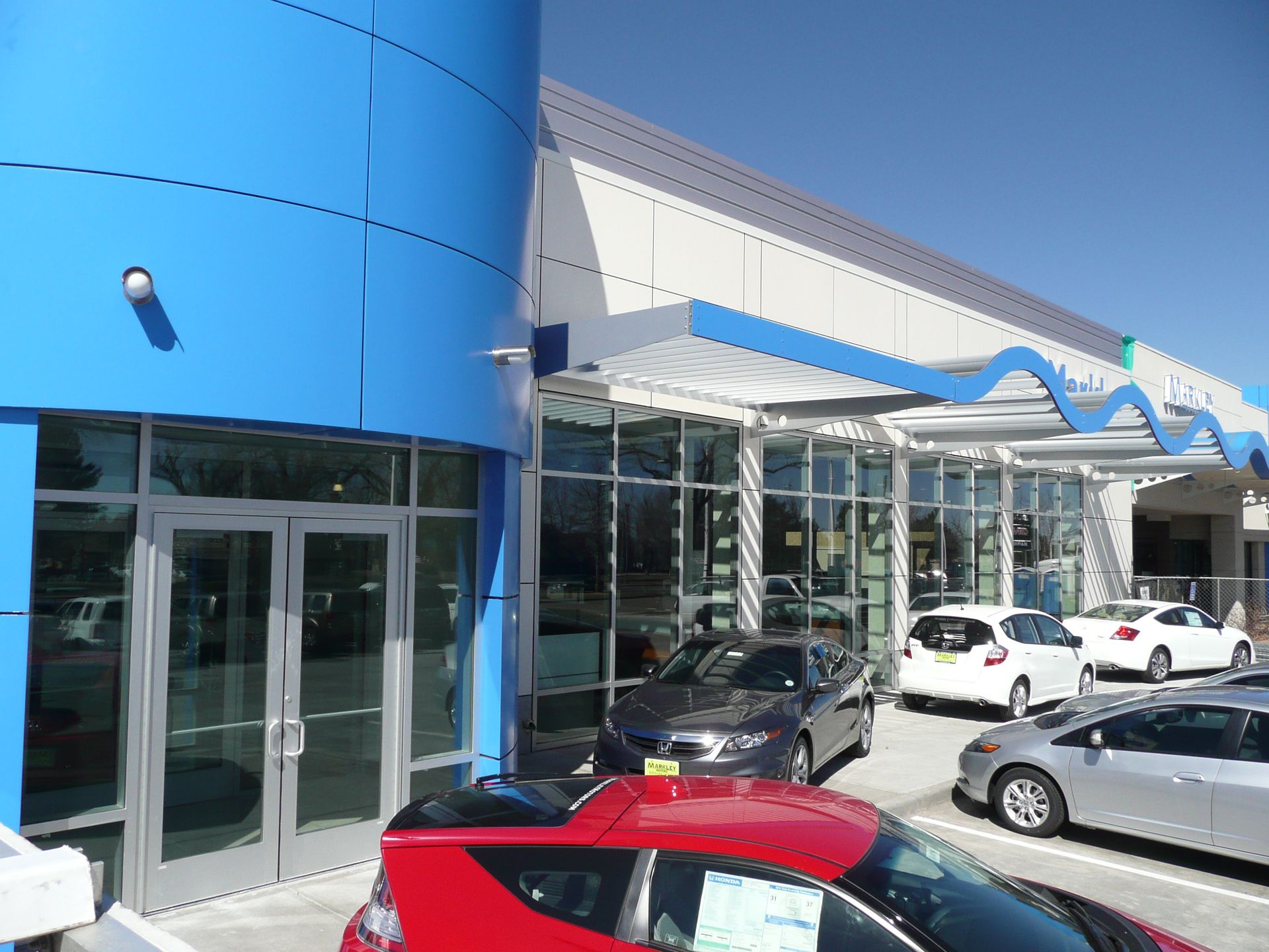 Modern commercial building with blue facade, glass entrance, and parked cars under a canopy