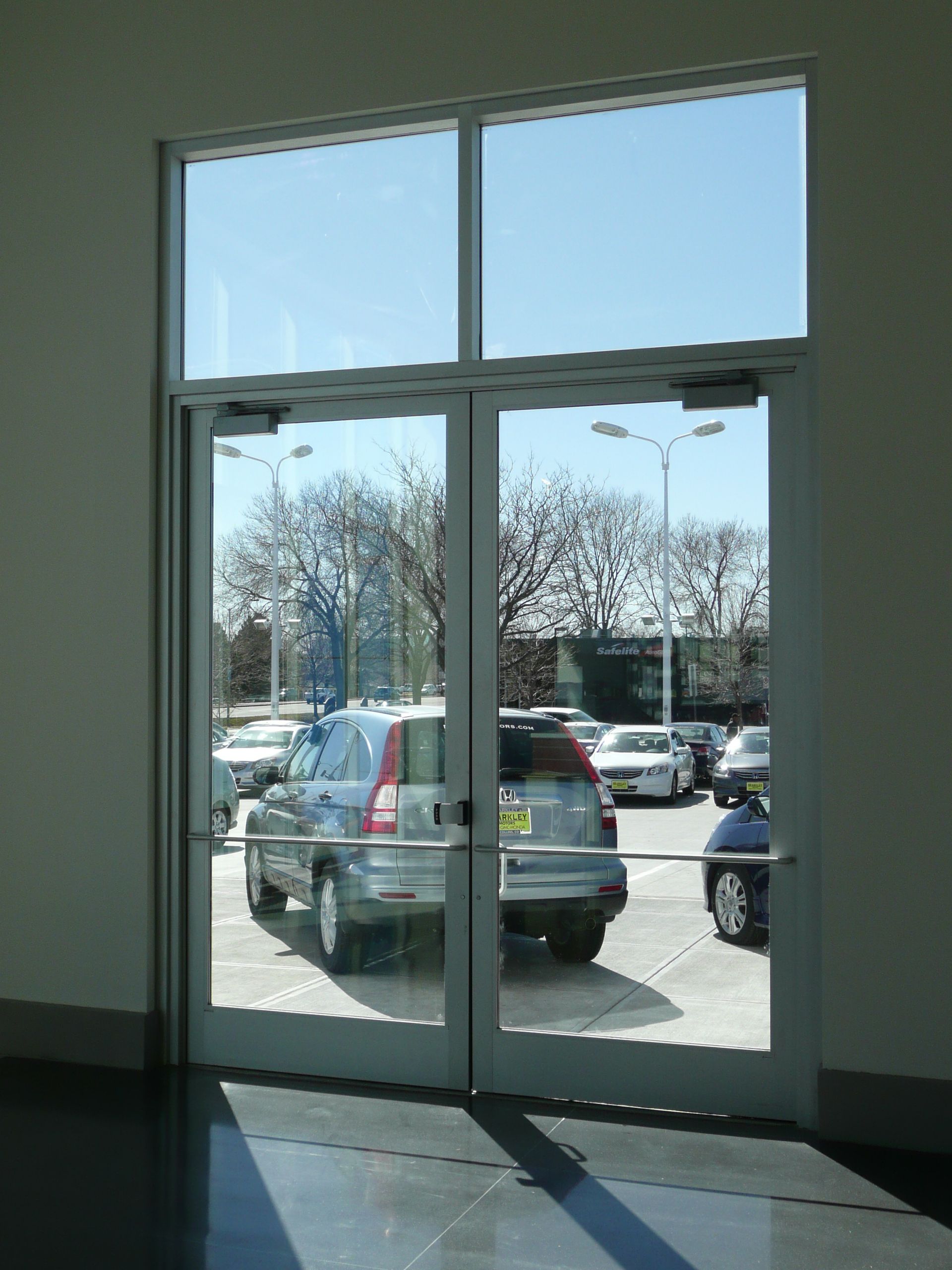 Glass door with parked cars visible outside in a sunlit parking lot