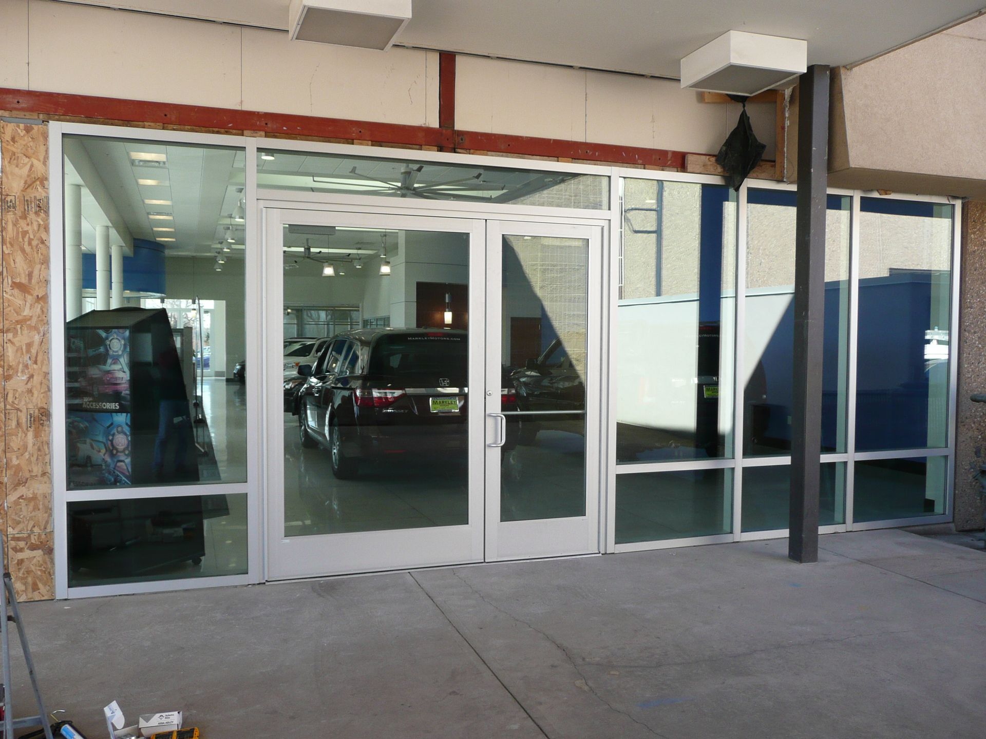 Glass storefront entrance with automatic sliding doors and parked cars visible inside.