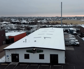 Aerial view of a white-roofed industrial building with a parking lot and snowy landscape at dusk