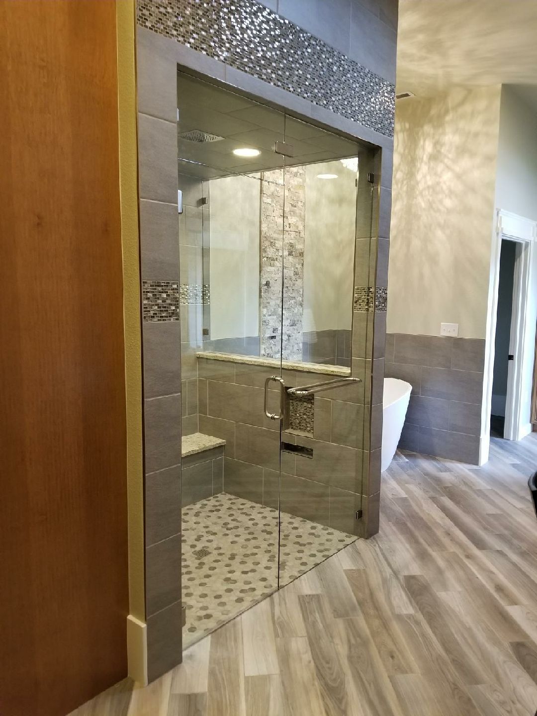 Modern bathroom with a glass shower enclosure, mosaic tile accents, and light wood-look flooring