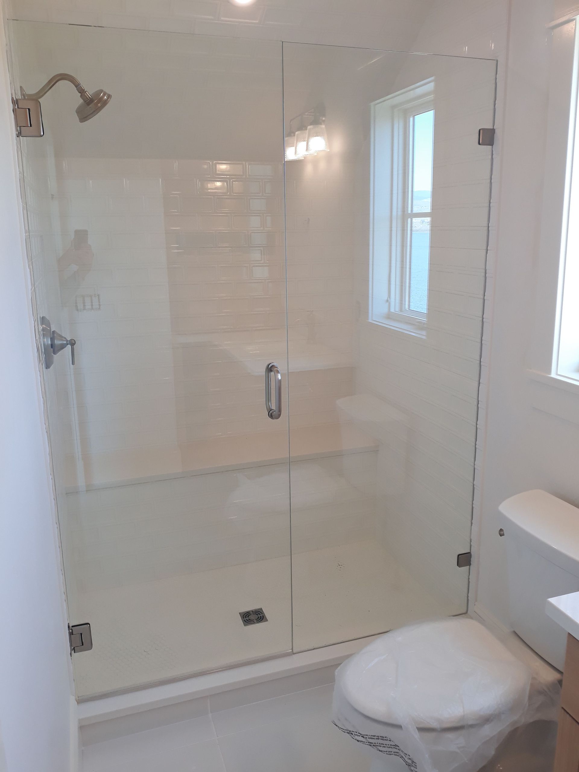 Glass-enclosed shower beside a toilet in a bright white bathroom