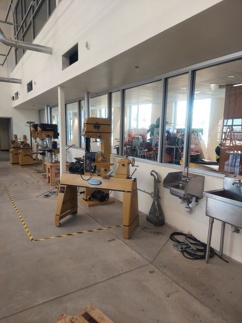Workshop with several drill presses and tools along a glass-walled corridor