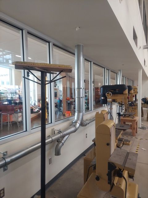Museum display of woodworking machinery and tools along a glass-walled corridor