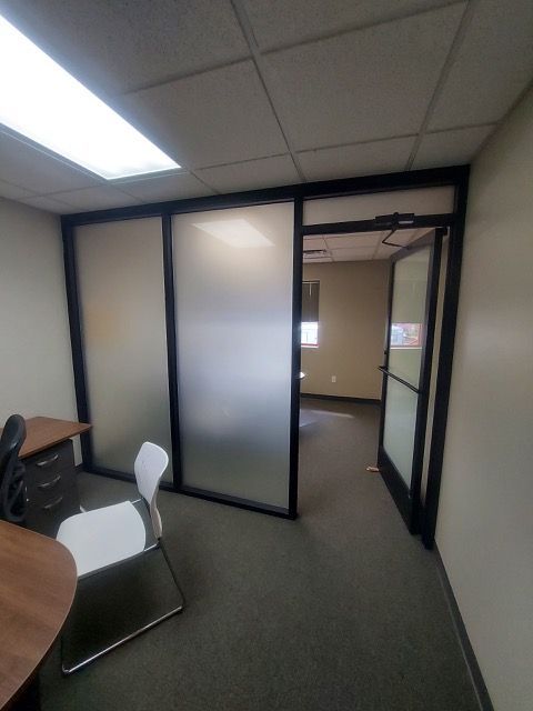 Small office with cubicles, frosted glass partitions, and an open doorway into a hallway.