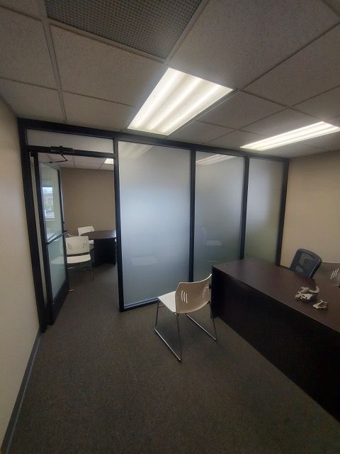 Office reception area with glass-walled rooms, black desk, and frosted partitions under fluorescent lights