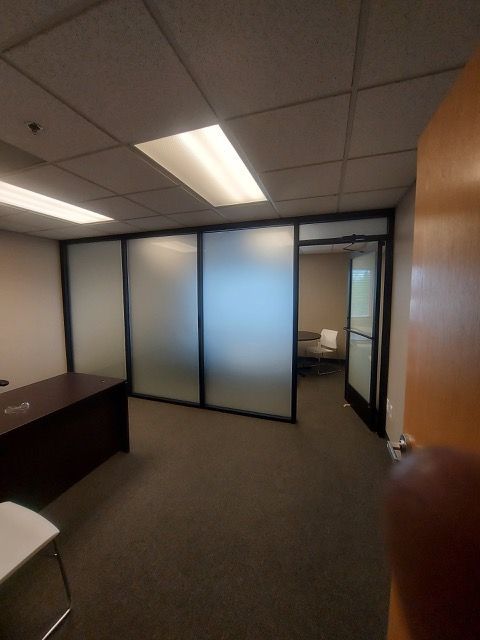 Empty office with frosted glass walls, desk on left, and an open doorway to a small room.