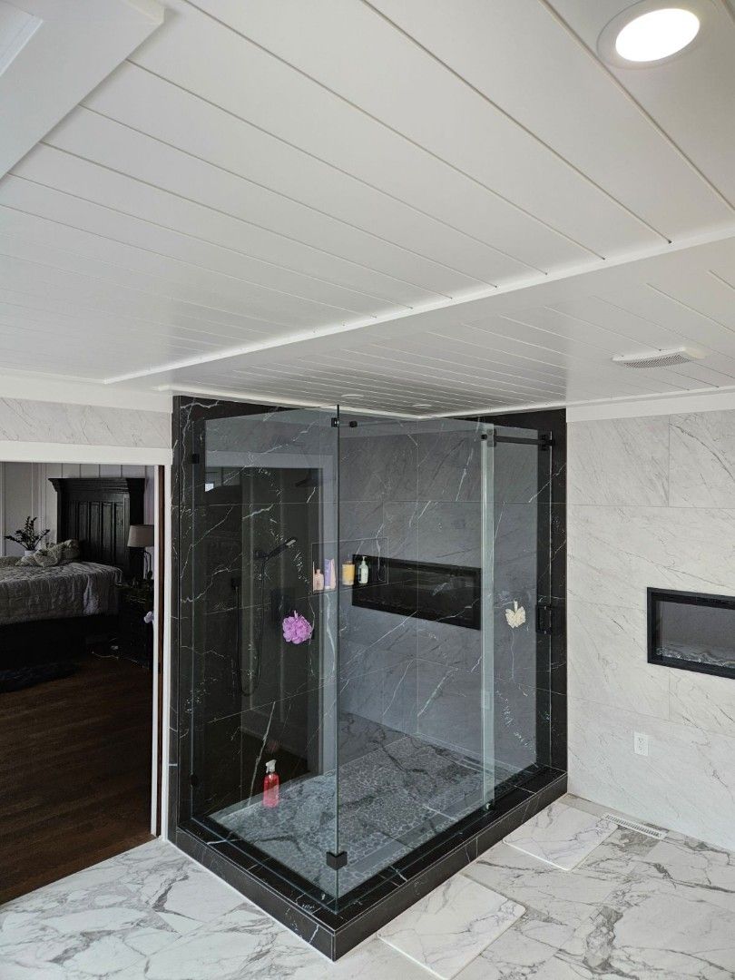 Modern glass shower enclosure in a white-tiled bathroom with black trim and a dark floor.