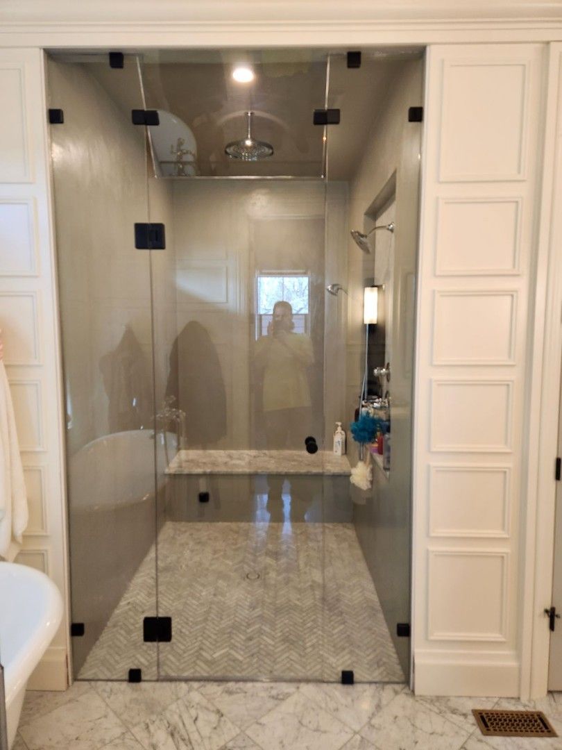 Glass-enclosed marble shower with rain showerhead and bench in a bright bathroom