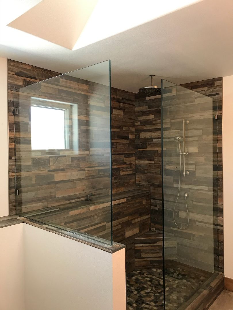 Glass shower enclosure with brown tile walls and a small window in a bathroom