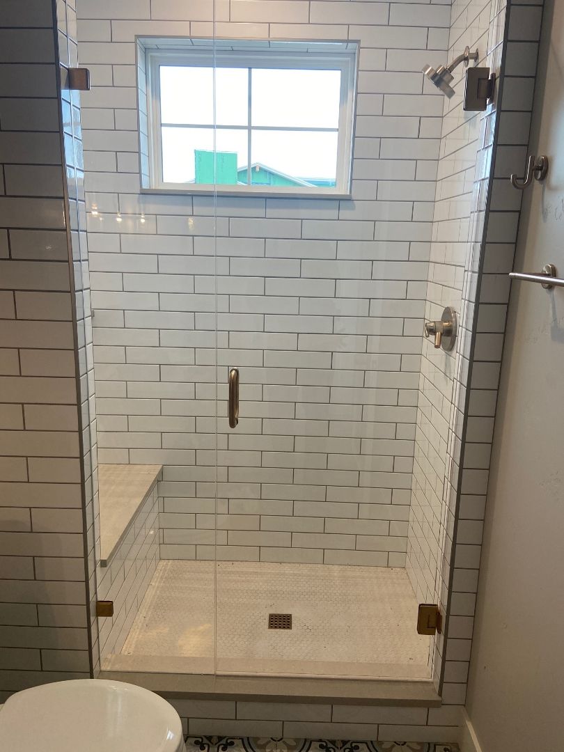 Tiled shower stall with glass door, white subway walls, and a small window above.