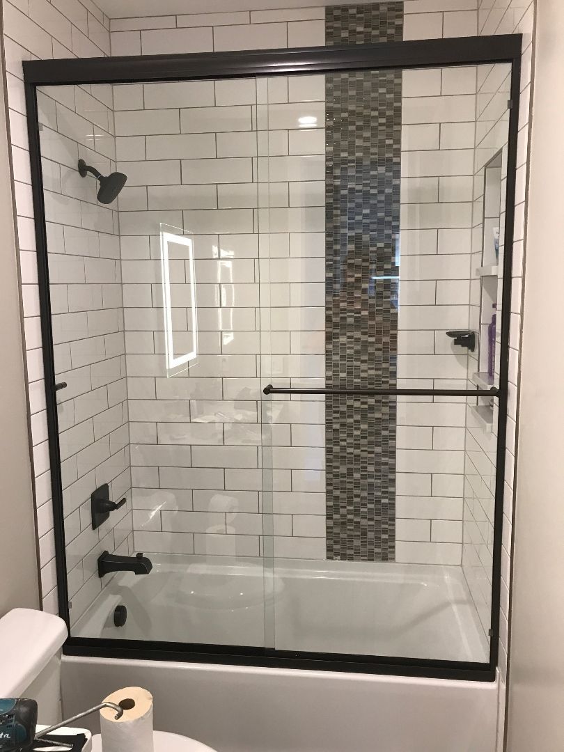 Glass shower with white subway tile and a dark vertical mosaic accent strip