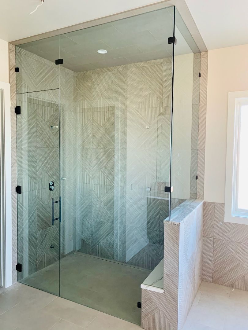 Glass walk-in shower with herringbone tile walls and a built-in bench in a bright bathroom