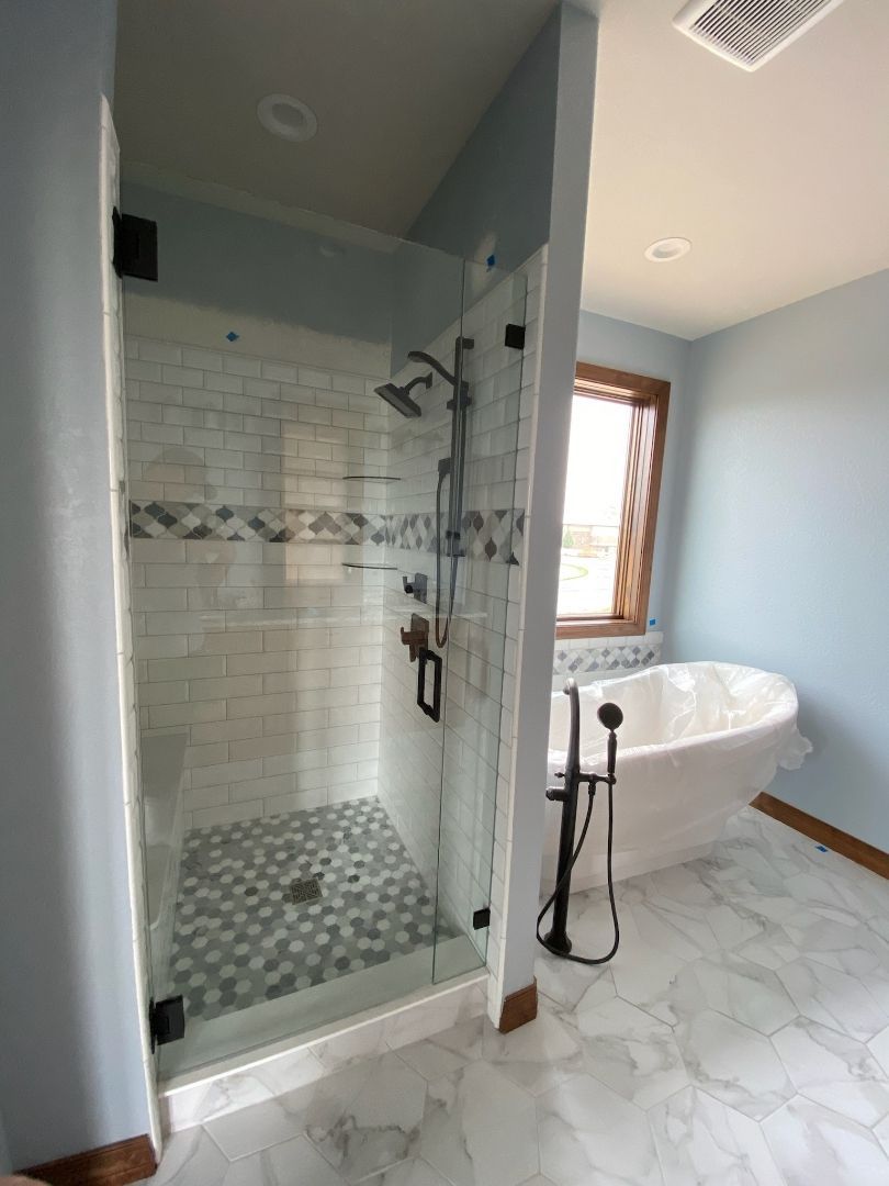 Modern bathroom with glass shower, white clawfoot tub, and tiled floor