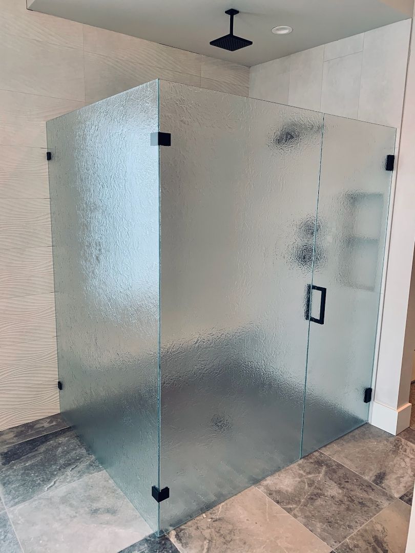 Frosted glass shower enclosure with black hardware in a tiled bathroom.
