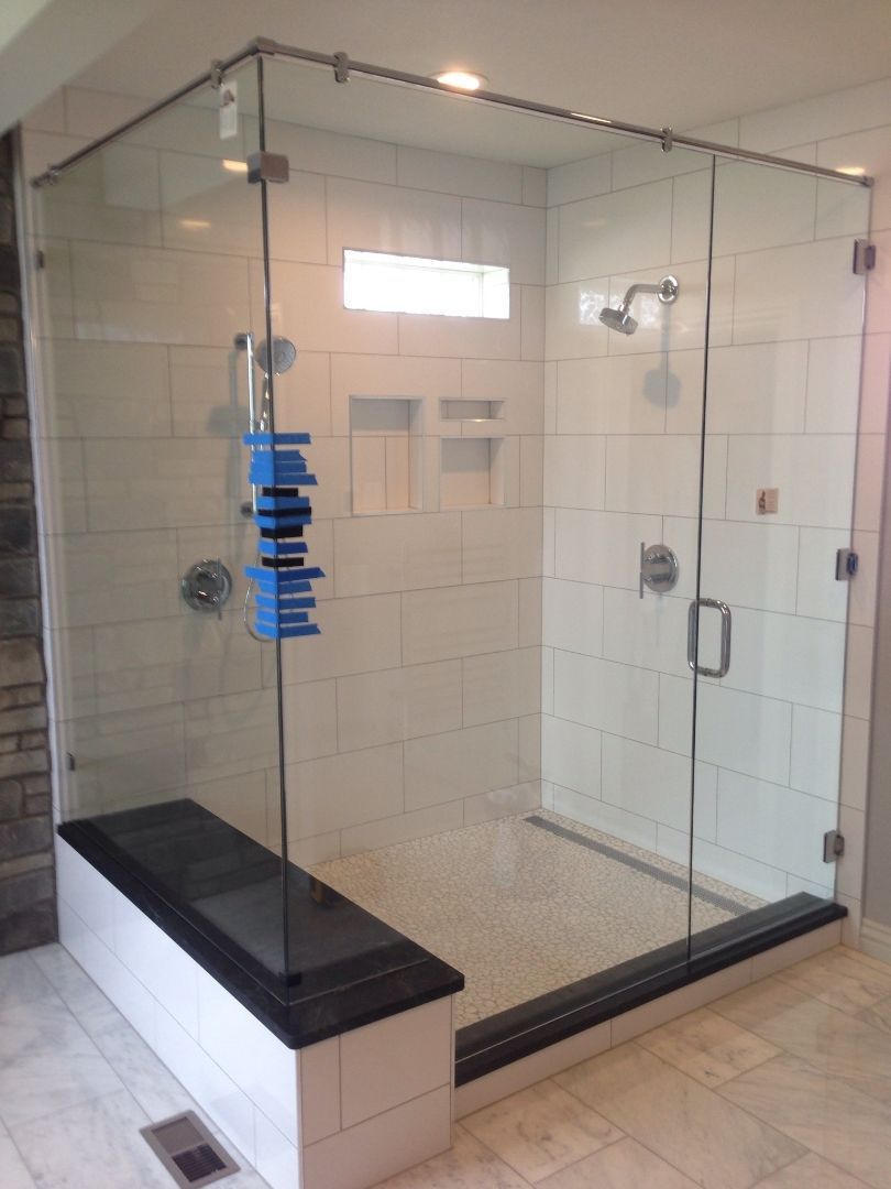Glass walk-in shower with black bench and blue shower caddy in a tiled bathroom