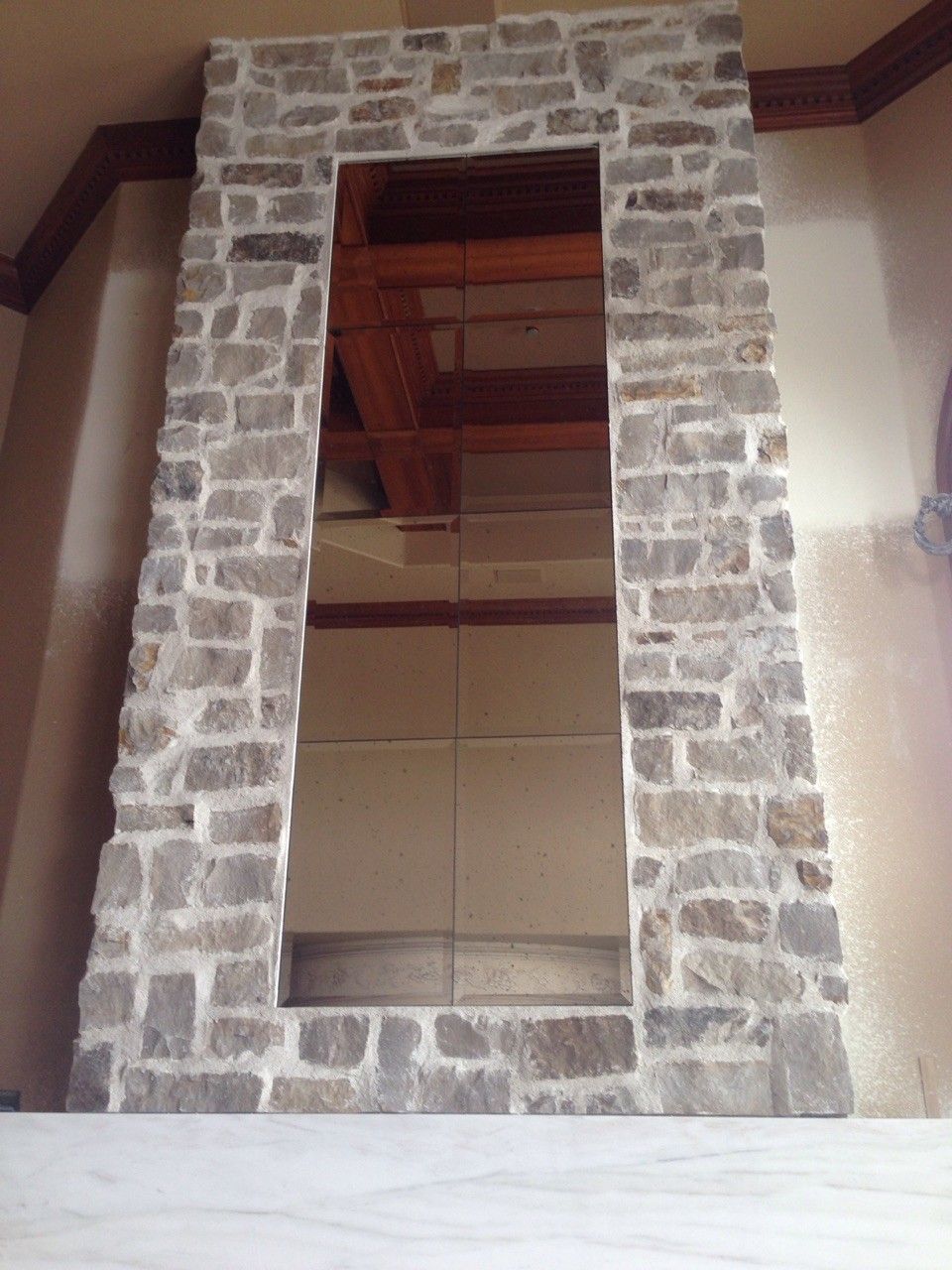 Stone-framed wall opening with a mirror reflecting a wooden ceiling inside a room