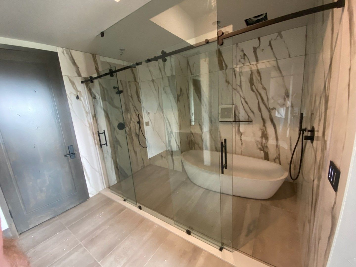 Modern bathroom with glass shower enclosure, marble walls, and a freestanding tub