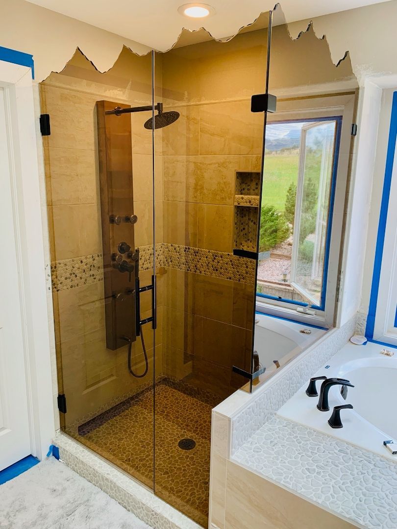 Modern bathroom with glass shower, tan tile, black fixtures, and a white vanity next to a window.